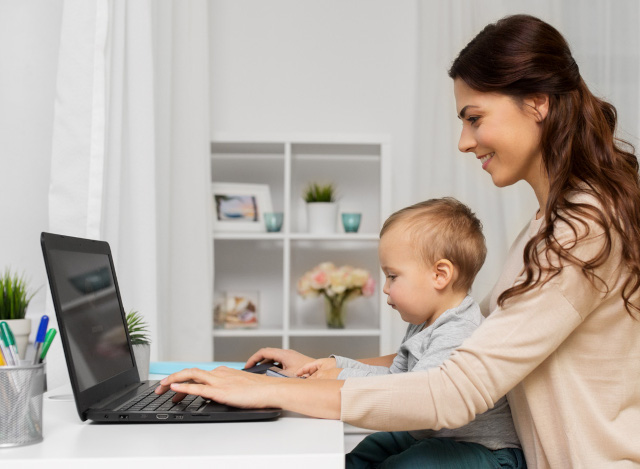 woman sitting with a child in her arms and writing on her laptop